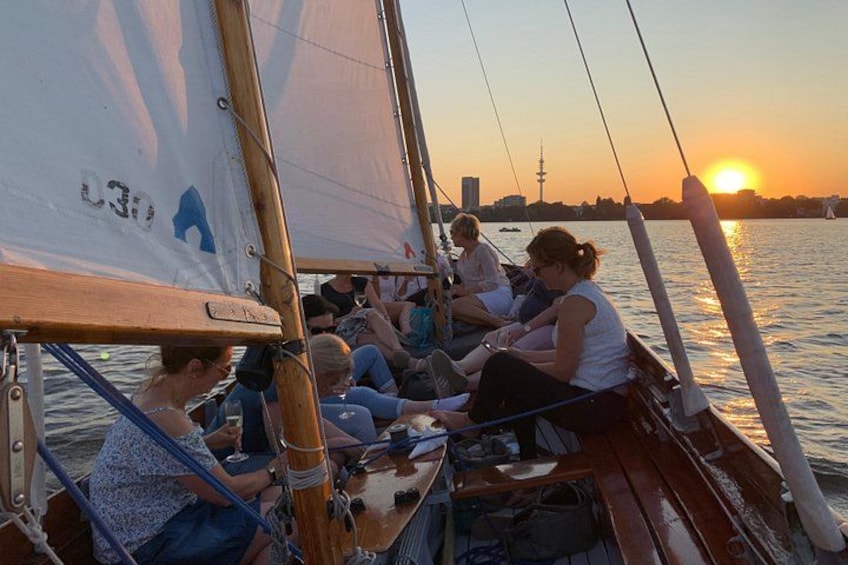 A sailboat with people on board, a sunset in the background, and a city skyline across the water. 4