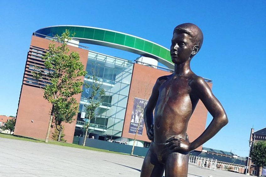Una estatua de bronce de un niño en una plaza pública con un edificio moderno al fondo. 5