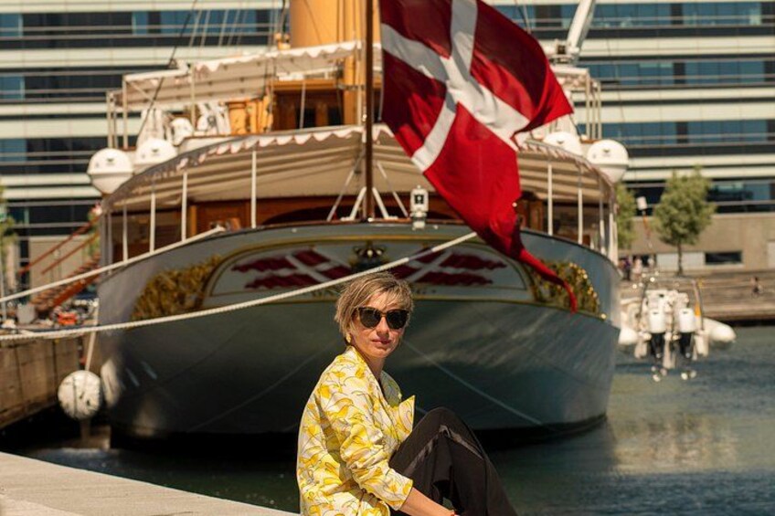 Una persona sentada junto a un muelle, con un barco grande al fondo que lleva una bandera roja. 2