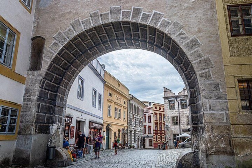 A stone archway in a cobblestone street with buildings on either side. 3