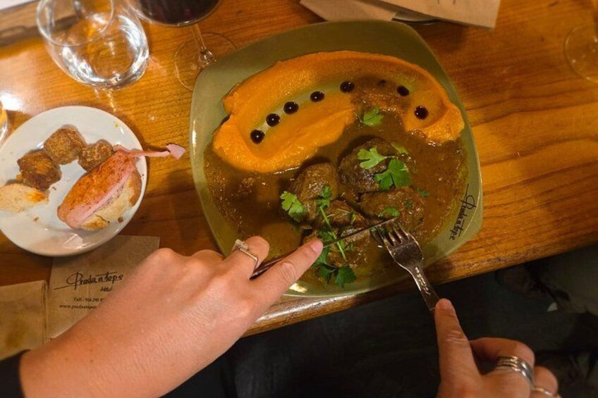 A plate of food with meatballs and a garnish, a glass of red wine, and a menu on the table. 2