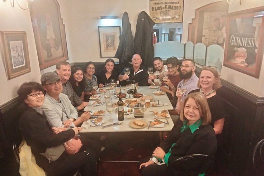 A group of people seated around a table in a restaurant with various dishes and drinks. 2