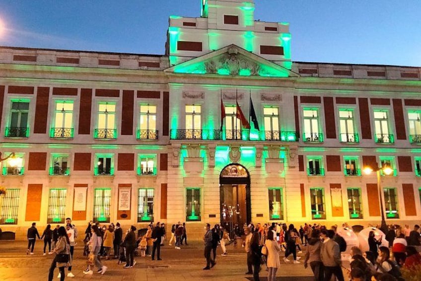 A large building with a central entrance and multiple windows, illuminated with green lights. 3
