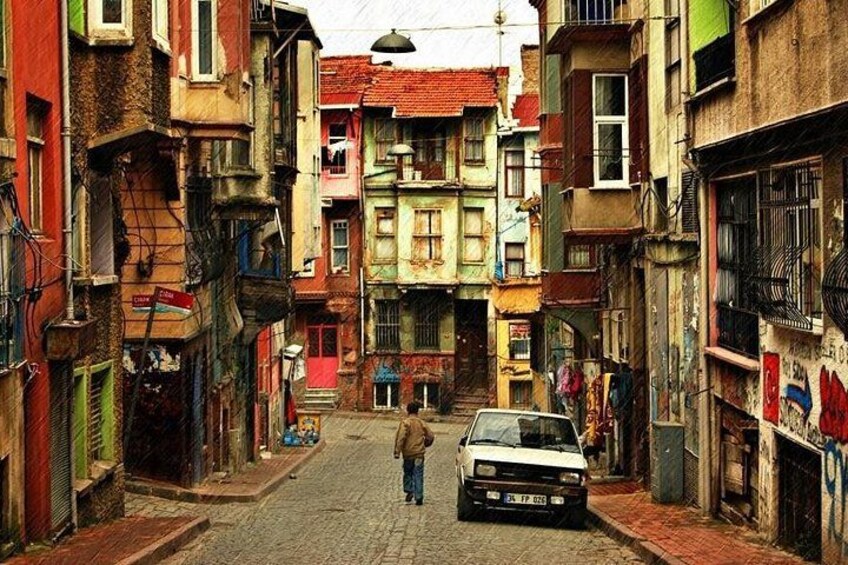 A narrow street with colorful buildings, a parked car, and a person walking. 3