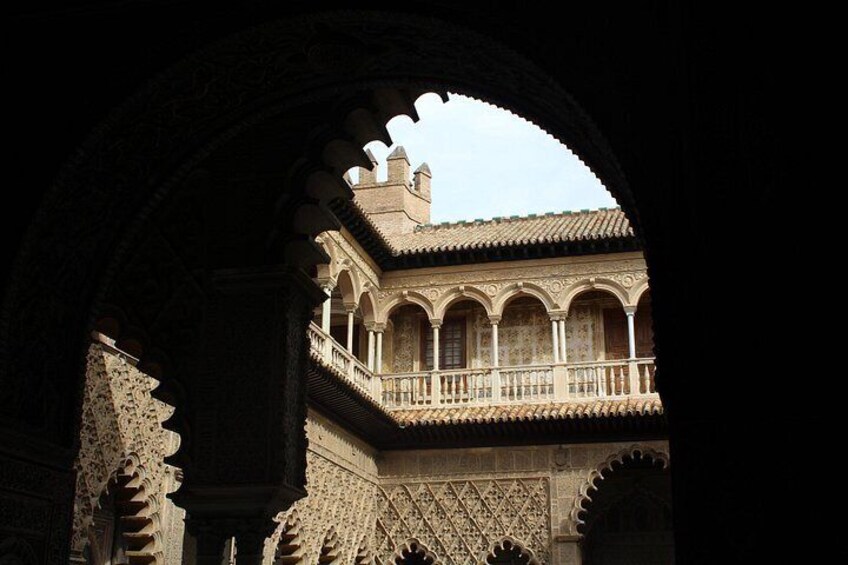Un arco de entrada que da a un patio con balcones ornamentados y detallada labor en piedra. 2