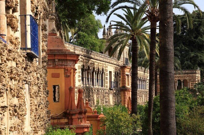 Un edificio histórico con arquitectura ornamentada, palmeras y un muro de piedra. 4