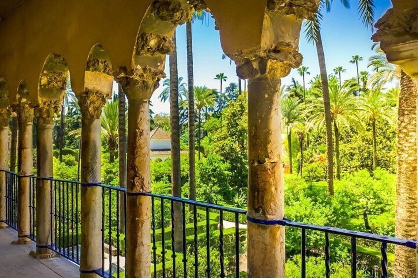 A covered walkway with columns, palm trees, and a well-maintained garden. 1