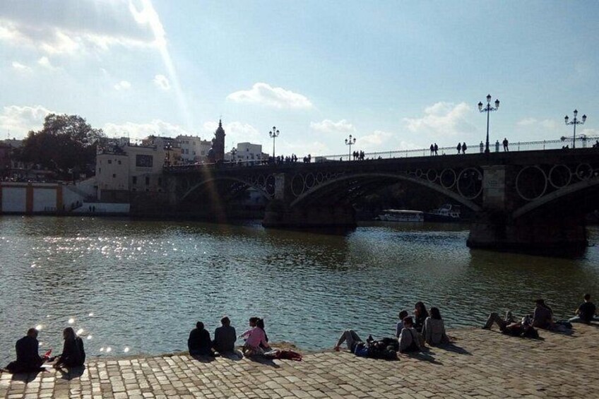 Un río con un puente, personas sentadas en la orilla y edificios al fondo. 4