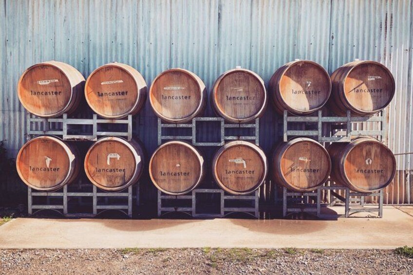 Des barriques en bois, empilées sur des étagères métalliques, sont adossées à un mur en métal ondulé. 2
