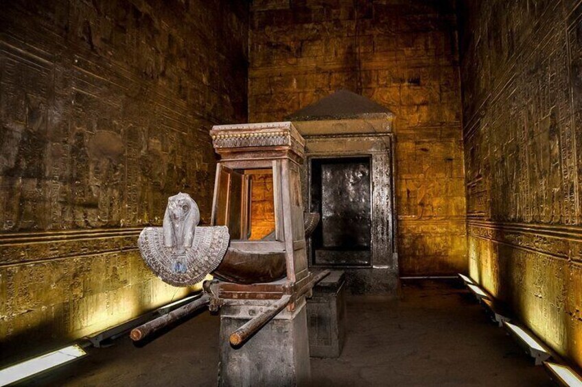 An ancient Egyptian sarcophagus with hieroglyphs, a wooden chest, and a stone door in a dimly lit room with stone walls. 2