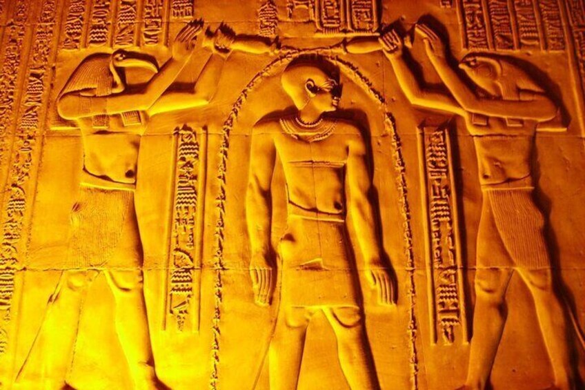 A relief sculpture of three figures with hieroglyphs and a central figure holding a staff. 1