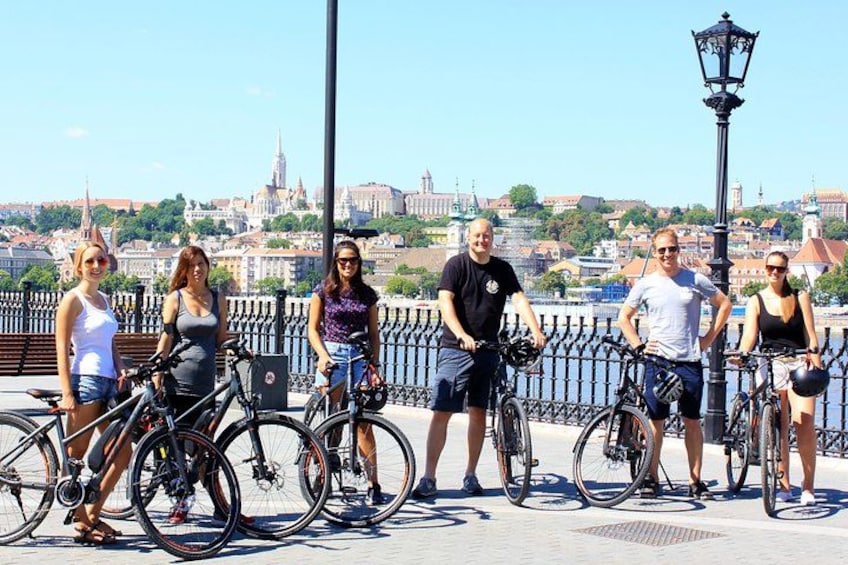 A group of people standing on a bridge with bicycles, overlooking a cityscape with historic buildings. 2