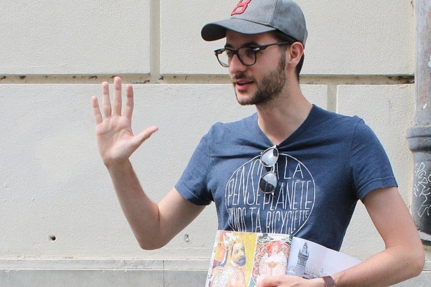 A person wearing a cap and a t-shirt with a graphic design, holding a book and gesturing with their hand. 3
