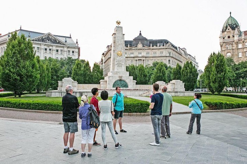 A group of people standing in a plaza with a monument and buildings in the background. 1