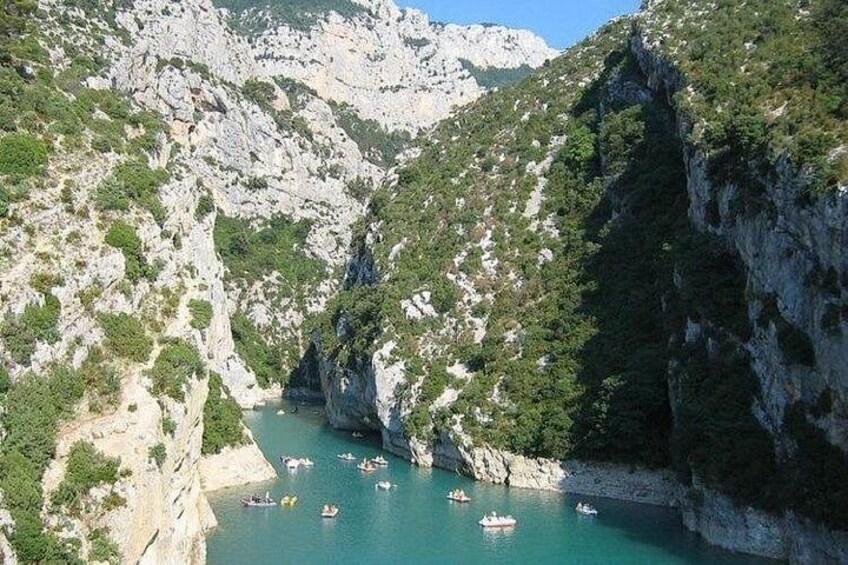 A canyon with boats on a turquoise river surrounded by rocky cliffs and greenery. 2