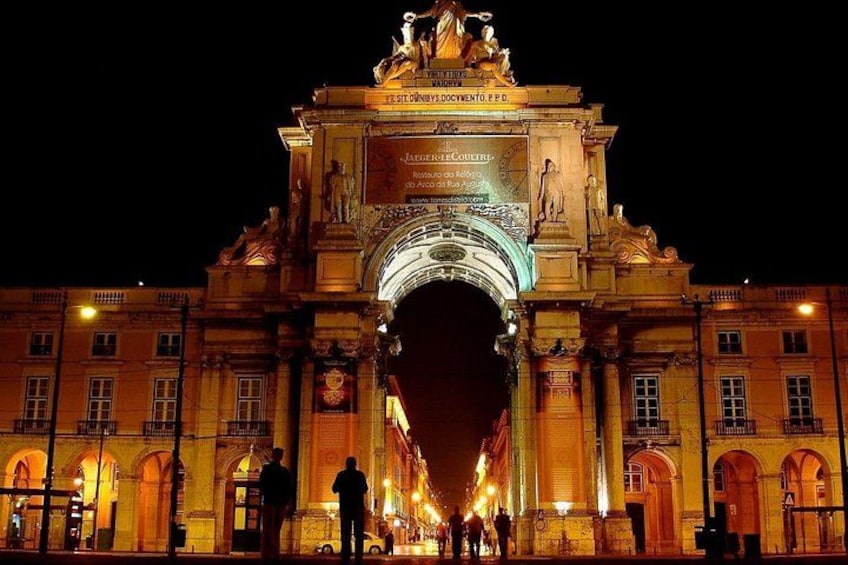 Un arco iluminado y monumental, con estatuas e inscripciones, rodeado de edificios. 1