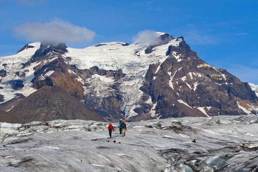 Un glaciar con dos excursionistas al frente y una montaña nevada al fondo. 5