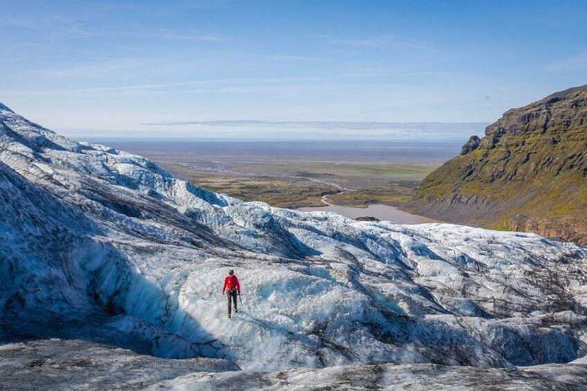 A person in a red jacket walking on a glacier with a distant view of a valley and mountains. 5