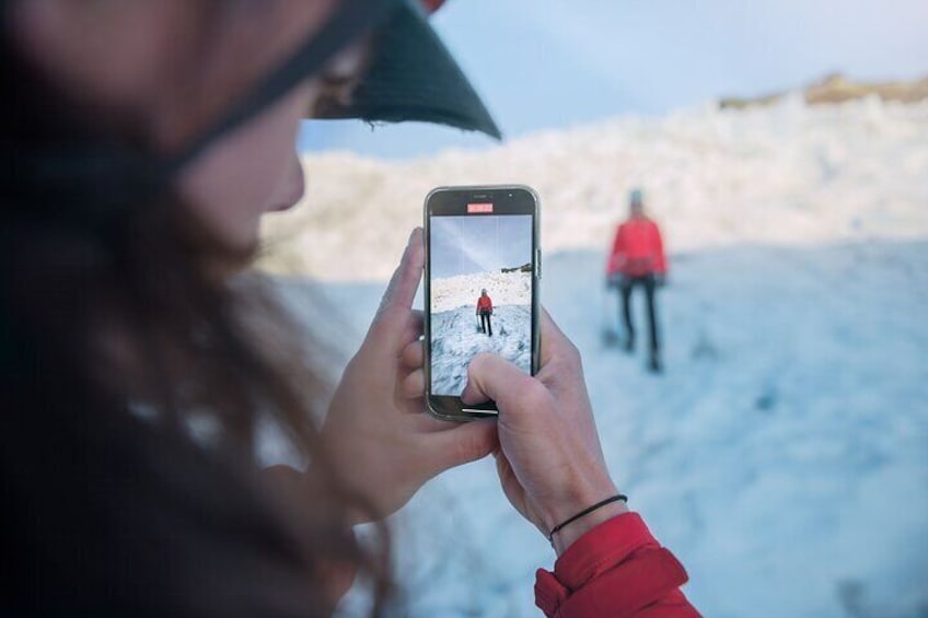 Una persona sosteniendo un teléfono inteligente, fotografiando un paisaje nevado con dos personas a la distancia. 2