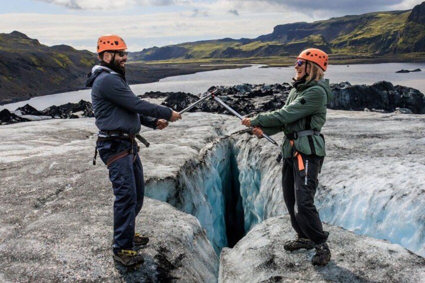 Two people rappelling down a glacier with a lake and mountains in the background. 1