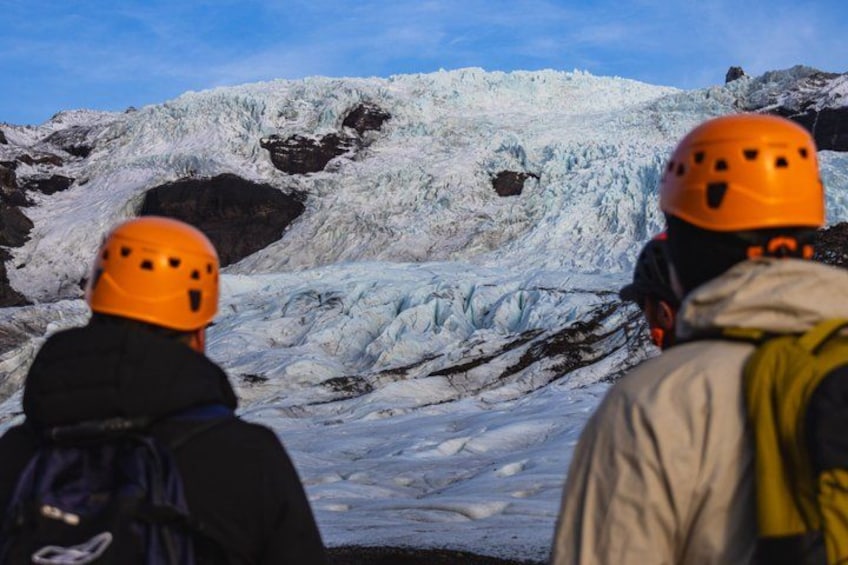 Two people wearing helmets observing a glacier. 4