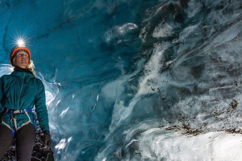 A person in a blue jacket and orange helmet inside a glacier cave. 1