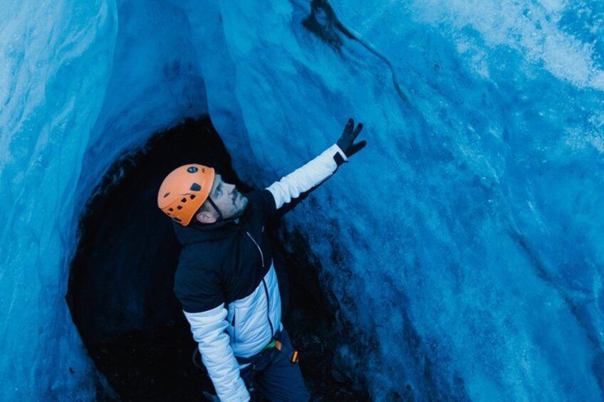 A person in a helmet and jacket inside a blue ice cave. 2