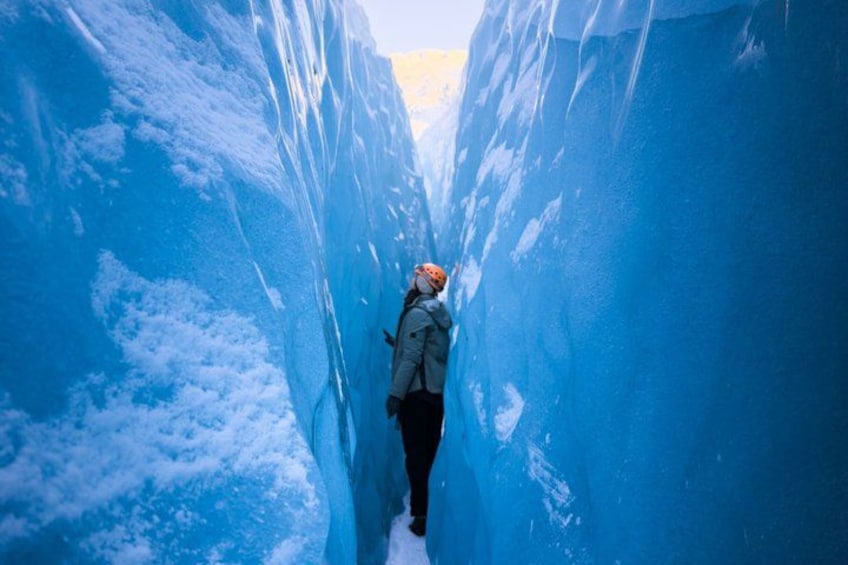 A person ice climbing in a narrow, deep blue ice tunnel. 2