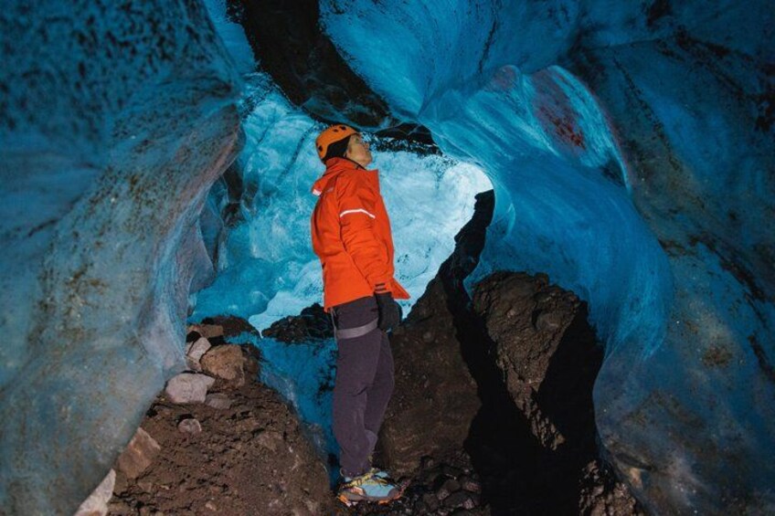 A person standing in a glacier cave with blue ice formations. 3