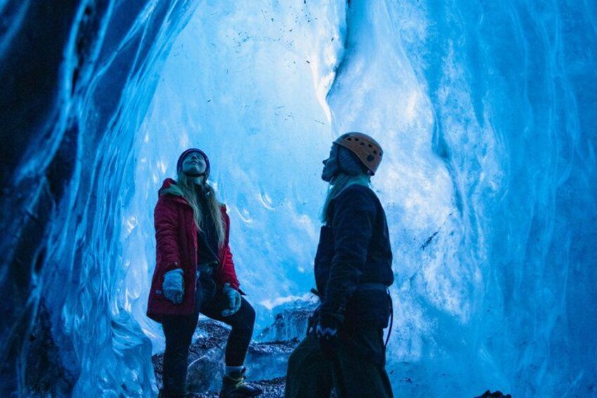 Two people inside an ice cave with blue ice formations. 1