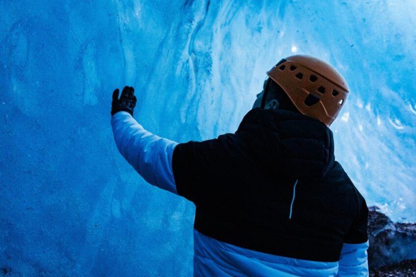 A person wearing a helmet and gloves, touching a blue ice wall. 5