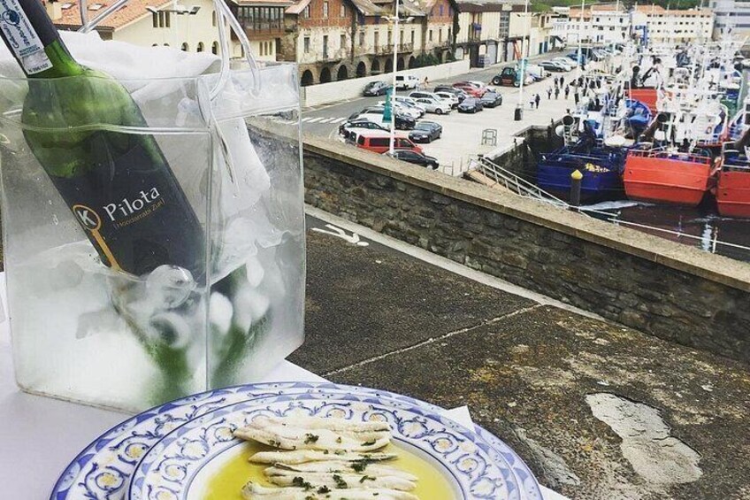 A bottle of Pilota wine, a plate with food, and a harbor with boats. 4