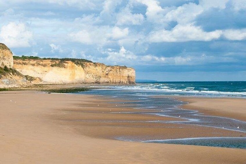 A beach with cliffs, waves, and a partly cloudy sky. 3