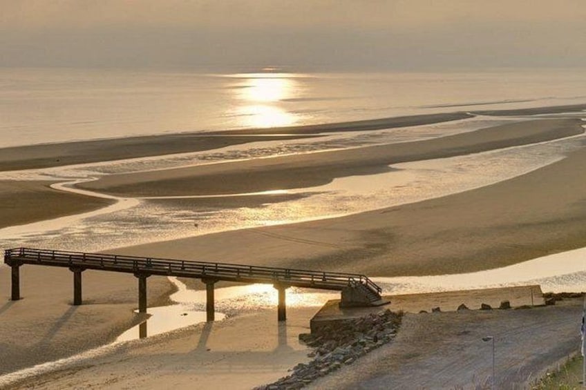 A coastal landscape with a bridge, sandy beach, and calm sea. 2