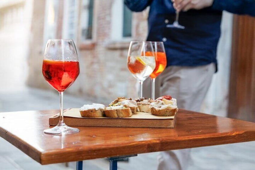 A wooden table with two glasses of red wine and a wooden board with pastries. 2