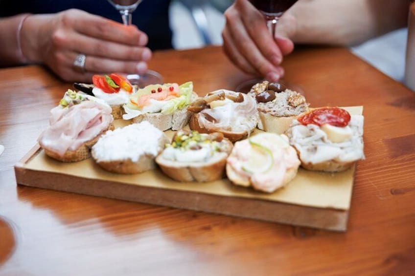Een houten plank met diverse etenswaren, waaronder sandwiches en hapjes, op een tafel. 4