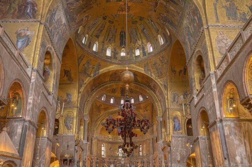 An interior of a grand cathedral with detailed mosaics, a large chandelier, and arched ceilings. 2