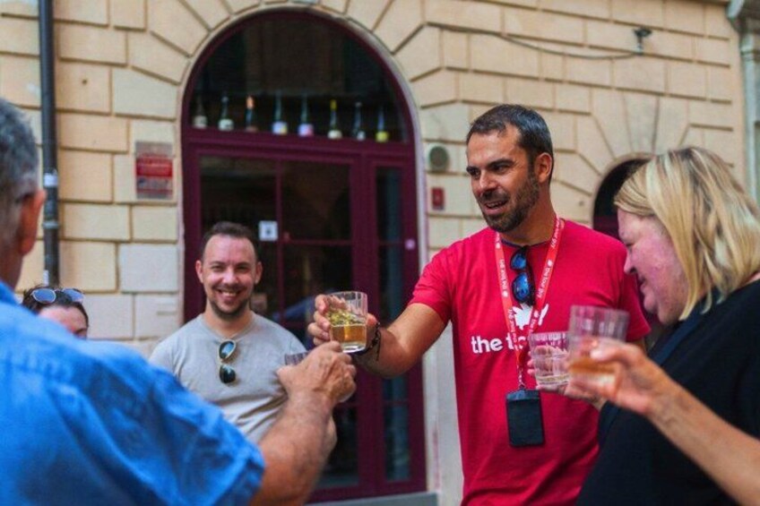 Une personne portant un t-shirt rouge et tenant un verre de bière, debout devant un bâtiment avec une porte rouge. 3