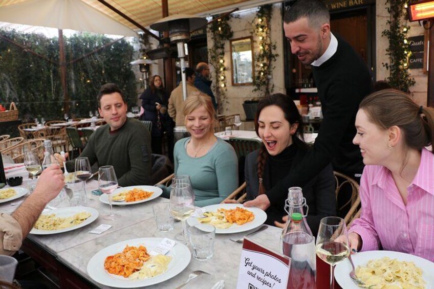 A group of people dining at an outdoor restaurant with tables, chairs, and a signboard. 3