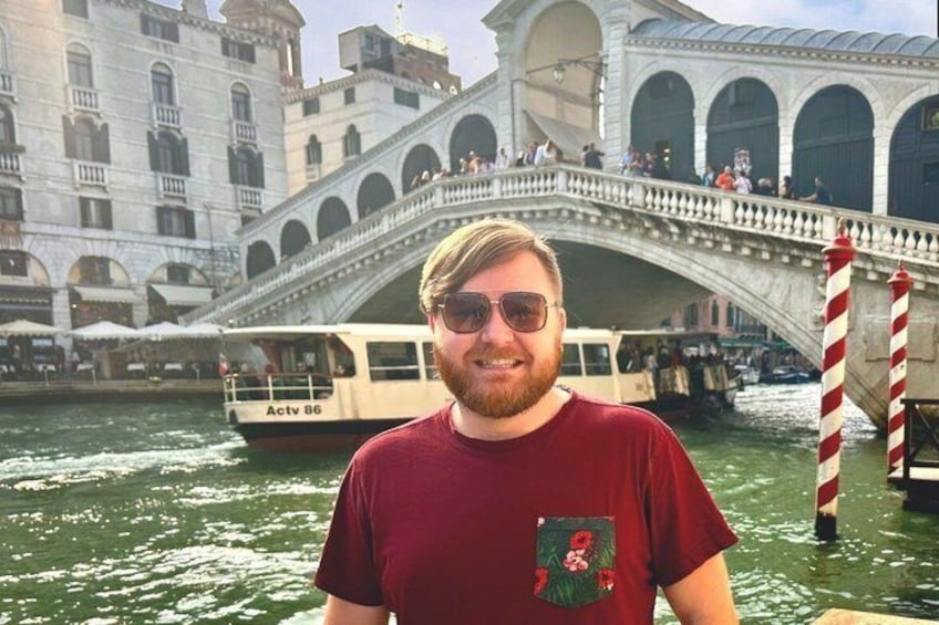 A person standing in front of a historic bridge with a boat in the background. 2