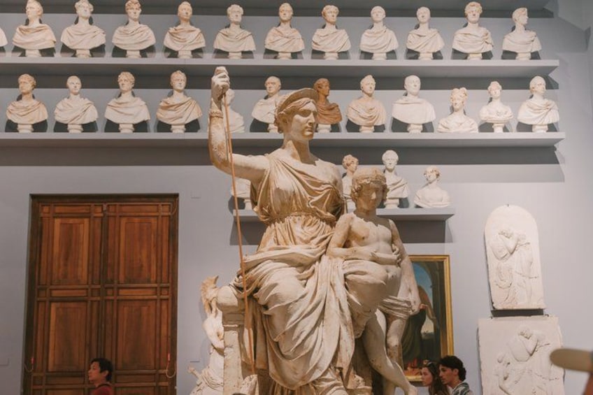 A marble statue of a woman holding a child, surrounded by other statues in a museum. 4