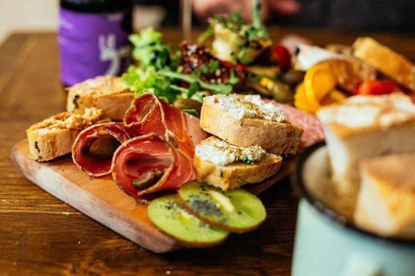A wooden board with various food items including sliced meats, bread, and vegetables. 2