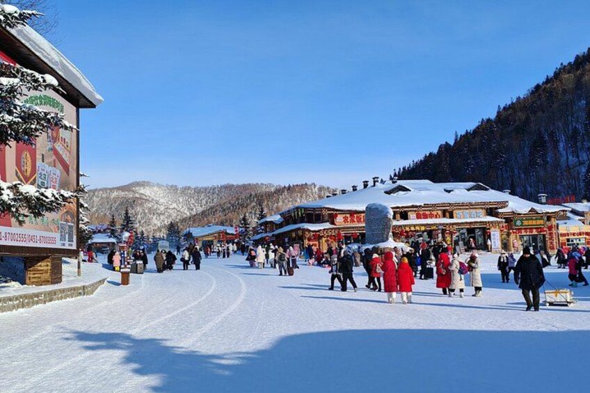 A snowy village with traditional buildings, a clear blue sky, and a mountainous backdrop. 3