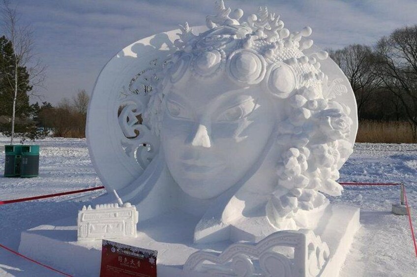 A snow sculpture of a woman's face with intricate details and a book titled 'The Snow Queen' at its base. 4