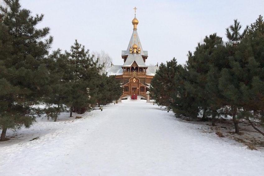 A snow-covered pathway leading to a wooden church with a golden dome. 1