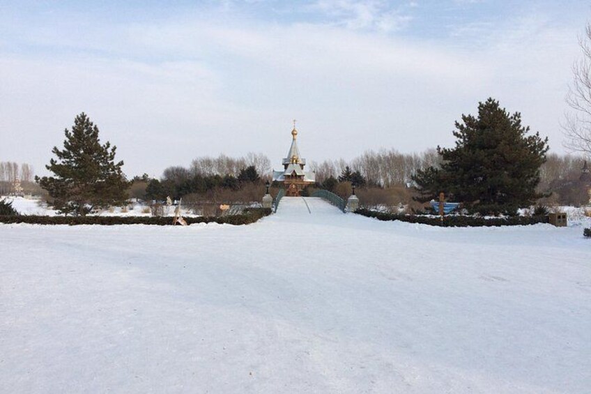 A snow-covered landscape with a large building featuring a golden spire, surrounded by trees and a stone wall. 2