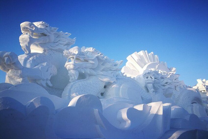 A snow sculpture of a dragon with intricate details and a clear blue sky in the background. 5