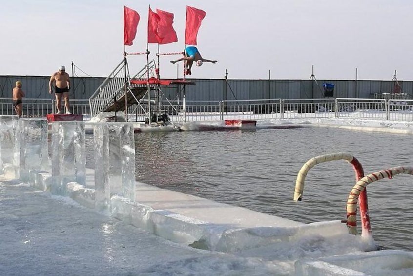 Eine Person taucht von einer Plattform in ein Becken mit Eisbarrieren. 1