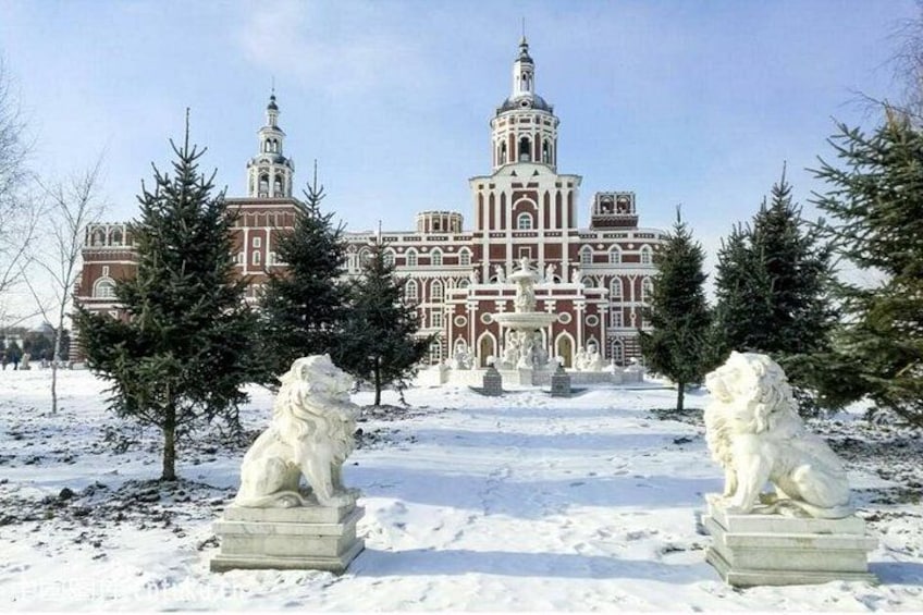 Eine schneebedeckte Löwenstatue, ein Gebäude mit Kuppeln und ein klarer Himmel. 2