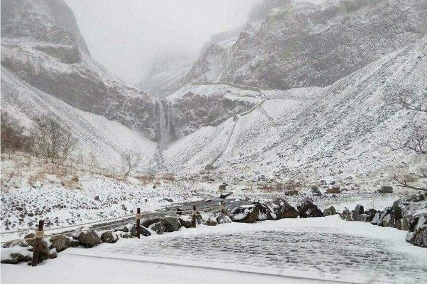 A snow-covered valley with a waterfall, rocky terrain, and a bridge. 2